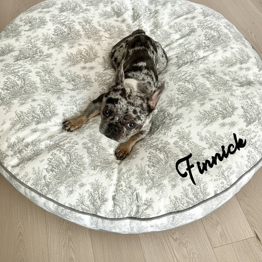 French Bulldog lying on a grey circular dog bed with a toile print and grey trim
