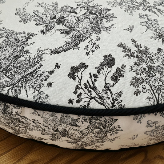 Close-up of a pet mattress with toile pattern and black border on a wooden floor.