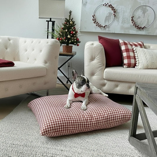 Dog sitting on a red checkered pillow in a living room with festive decorations.