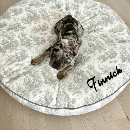 French Bulldog lying on a grey circular dog bed with a toile print and grey trim